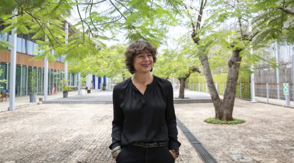 A person standing confidently in a green urban surrounding with hands in pockets.