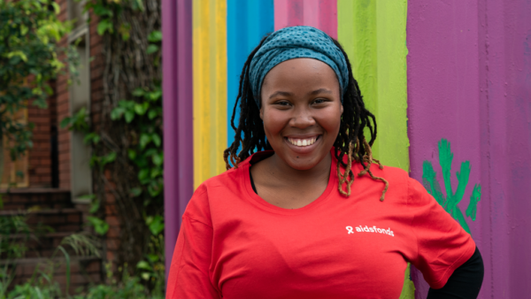 Portrait of Manelisi, community care worker in South Africa, wearing a red t-shirt in front of a colorful wall