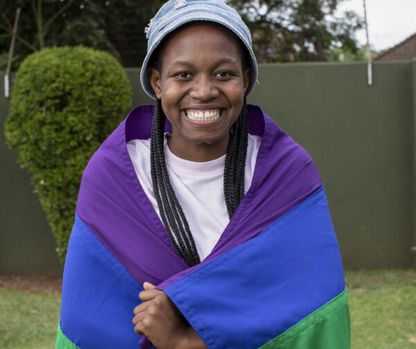 Girl wrapped in a rainbow flag smiling into the camera