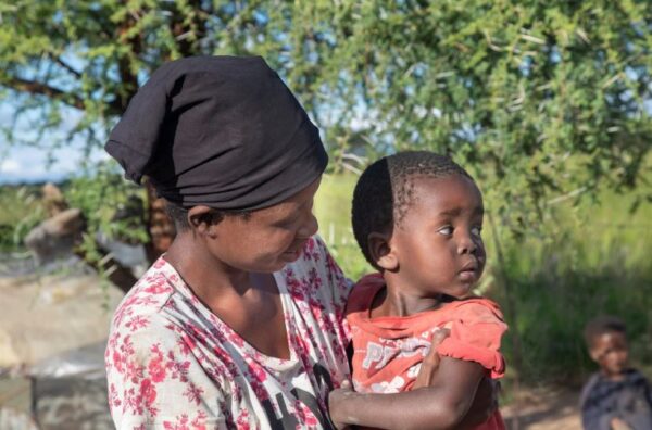 Woman with a black scarf on her head carrying a child in a red shirt who is looking away