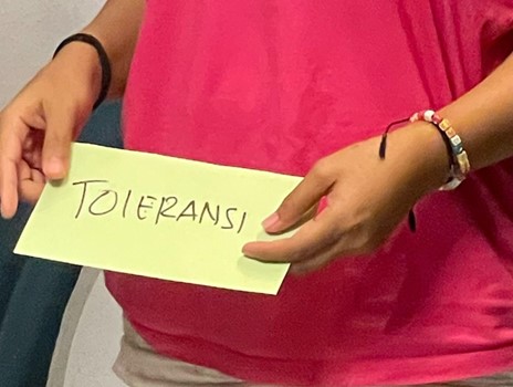 Person holding a green paper with "TOLERANSI" written on it.