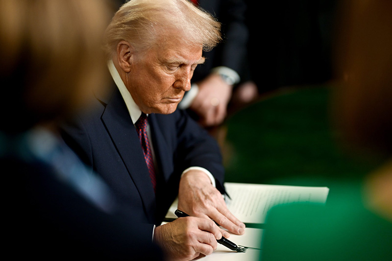 Trump seated at a desk, signing a crucial document with focused intent