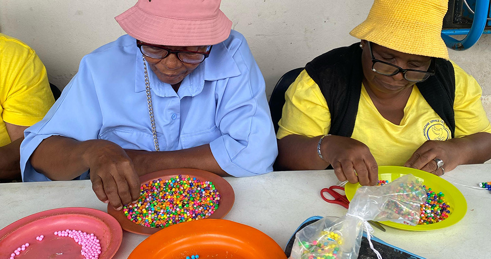 Two people in hats engage deeply in learning across borders, meticulously sorting colorful beads on trays at a table.