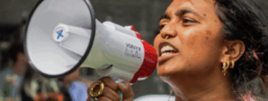 A person holding a megaphone speaks passionately at an outdoor event.
