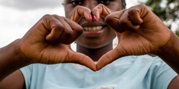 A person smiles while forming a heart shape with their hands in front of their face.