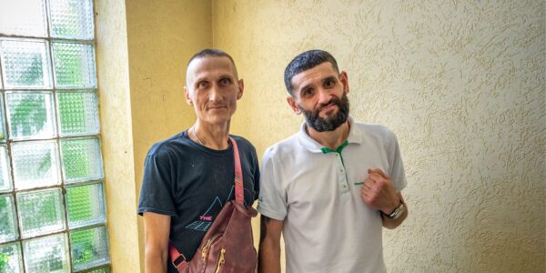 Davyd and Dmytro stand indoors by a glass-block window.