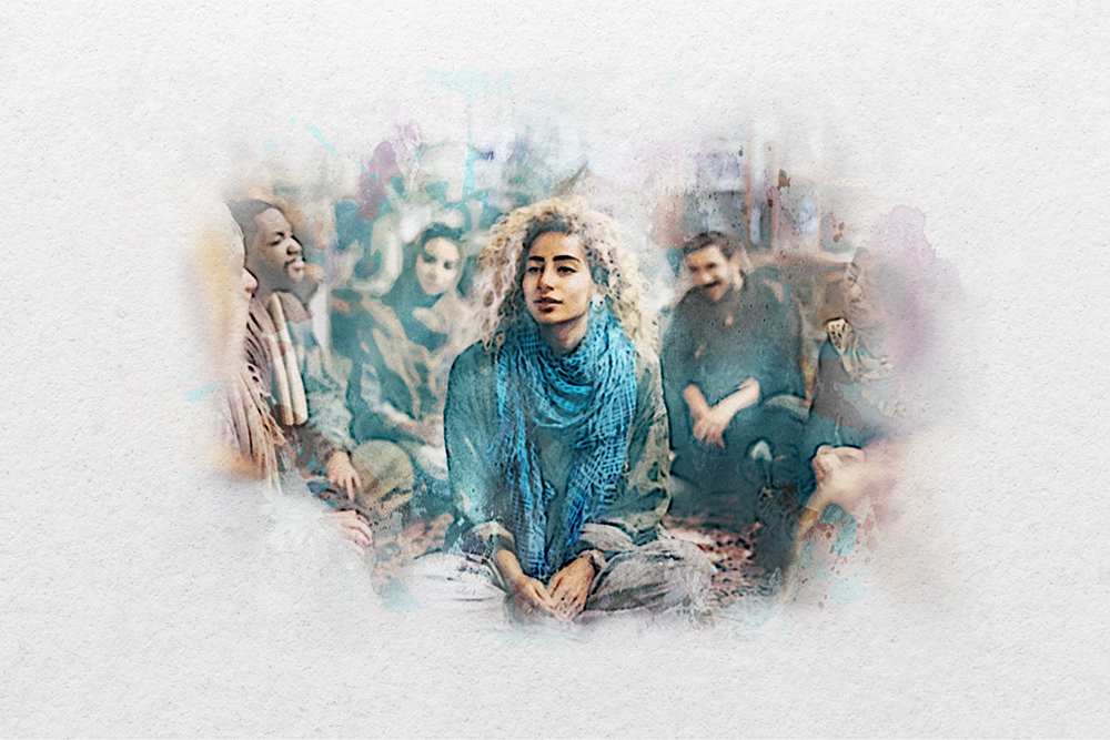 A group of people sit together indoors, with one person wearing a blue scarf seated in the center, all appearing engaged in conversation.