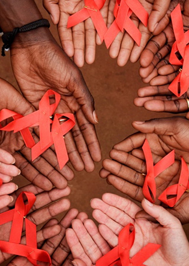 A group of diverse hands holding red HIV/AIDS awareness ribbons, arranged in a circle on a brown surface.